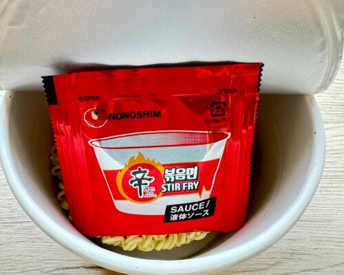 蓋を開けたカップの中。乾燥した麺の上に液体ソースの袋が入っている様子。