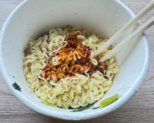 湯切りした白い麺の上に、真っ赤な液体ソースをかけた状態。カプサイシンの刺激的な香りが立ち上がる瞬間。